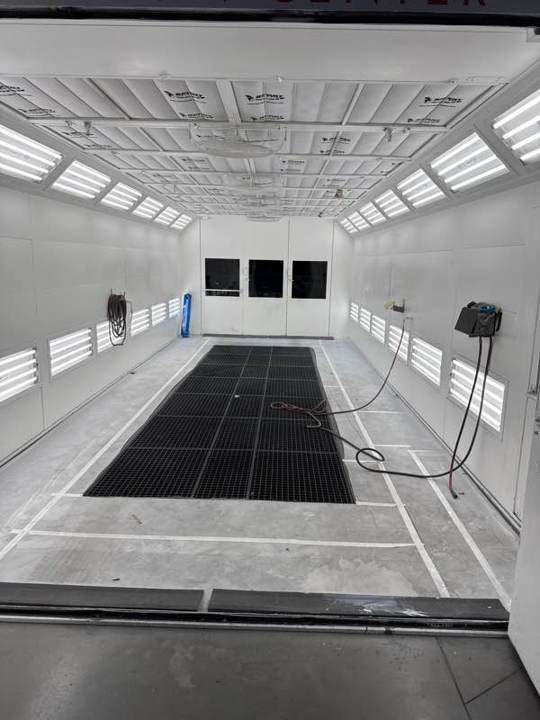 Clean downdraft paint booth with fresh floor filters and bright side lights after a service visit