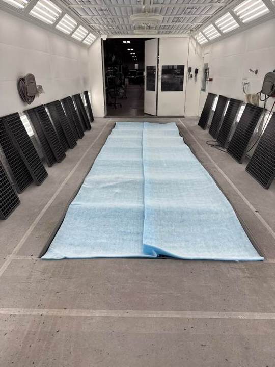 New blue floor filters laid across the pit of a downdraft booth during a filter change